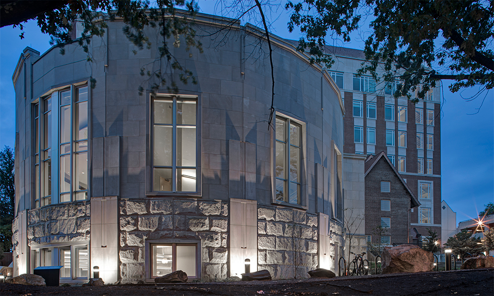 <p>View of the Team-based Active Learning Classroom at night from the east under preserved old growth oak trees, with the renovated section of Strong Hall dorm in the the distance.</p>
