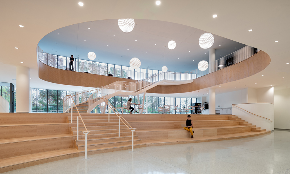 <p>The building’s most heavily used spaces are organized around a central two-story atrium, creating a vibrant hub that encourages interaction and collaboration. Overlooking the lobby, the student café is prominently positioned a few steps above, activating the heart of the building. Designed to transition from a vending lounge to a full vendor-operated food service as enrollment grows, the space supports both immediate needs and the project’s long-term vision for a dynamic campus community.</p>
