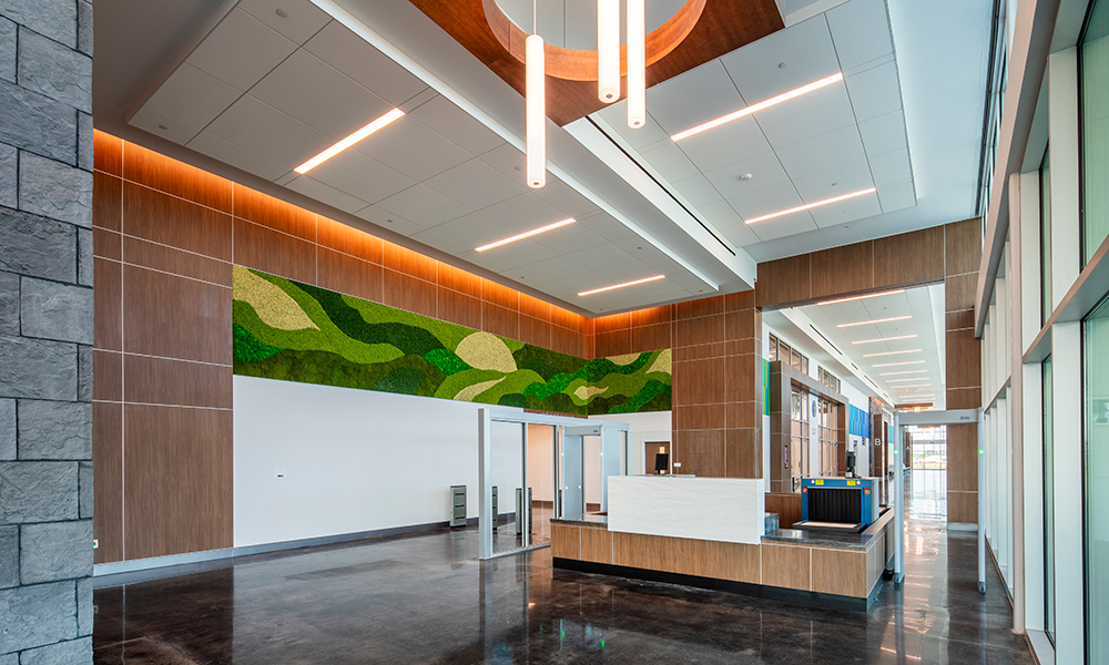 <p>Preserved moss wall installations inspired by the County’s official logo, paired with a linear arrangement of felt acoustical panels, create an immersive environment where occupants can experience a subtle, encoded representation of the County’s brand identity as “Florida’s Crossroads of Opportunity,” reinforcing a sense of place and community pride.</p>
